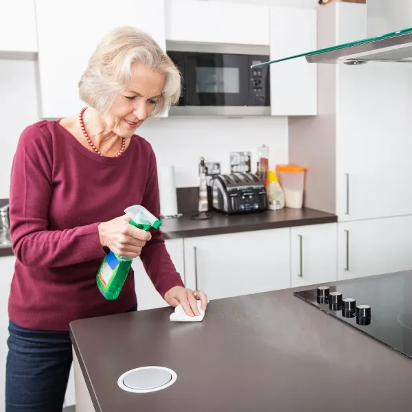 An elderly woman spring cleaning the kitchen countertop