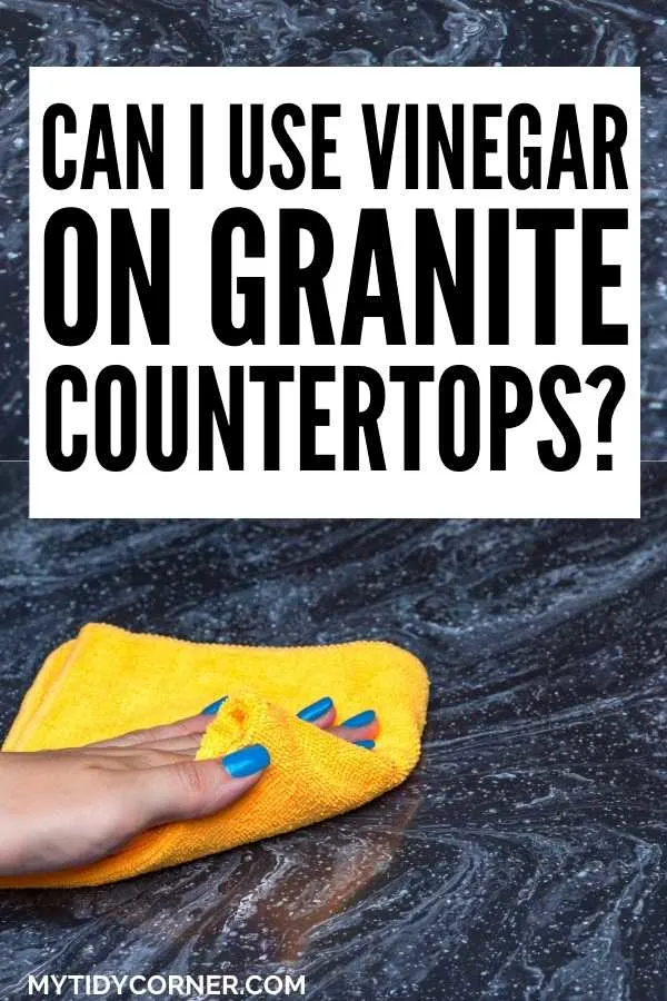 A hand holding a yellow rag on a black countertop with text that says, "Can I use vinegar on granite countertops?"