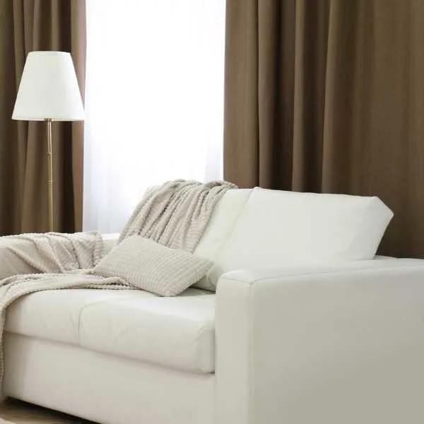 White sofa and lamp in front of brown curtains.