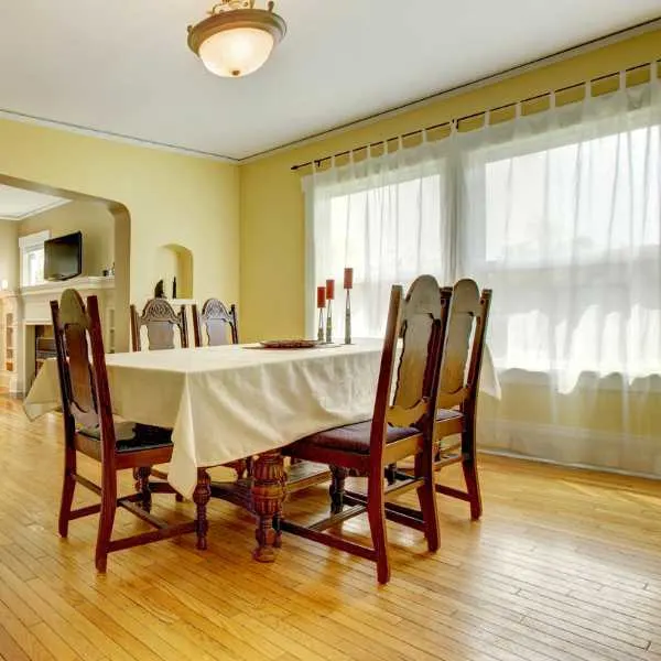 A dining room with yellow walls and white curtain.