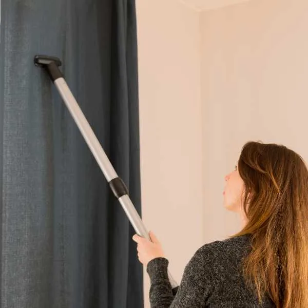 A woman vacuuming a curtain.