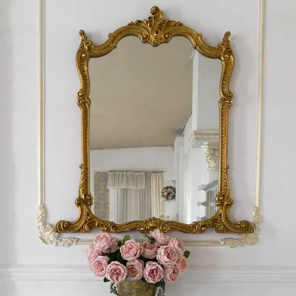 Mirror with fancy golden frame on a wall and flowers.