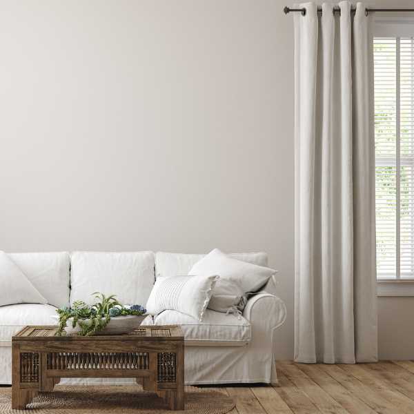 Neutral living room with white couch, coffee table, white wall and cream curtain.