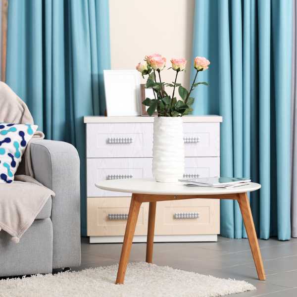 Room with couch, throws, table, dresser flower and blue curtains.