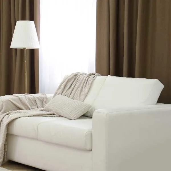 White couch, lamp and brown curtains.