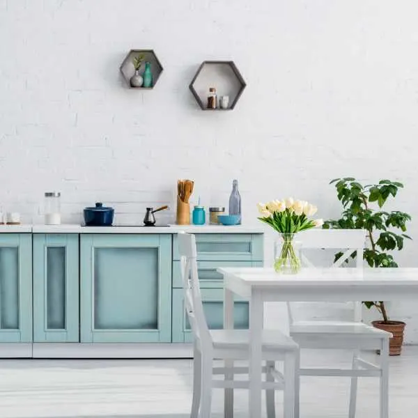 Beach inspired kitchen with blue cabinets, white dining table and chairs, flower on the table and a large plant.