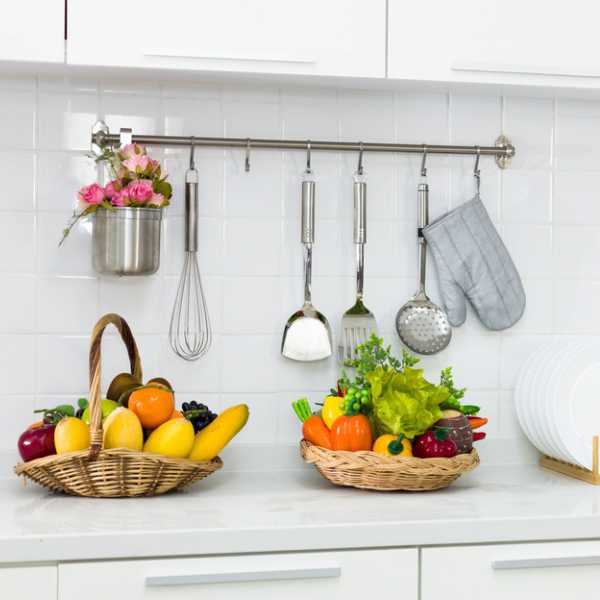 Kitchen with baskets of fruits on counter, flower bouquet and utensils hanging on the wall.