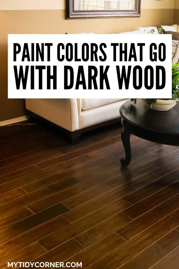 Living room with cream wall and couch, wood floor, coffee table and text overlay that says, "Paint colors that go with dark wood".
