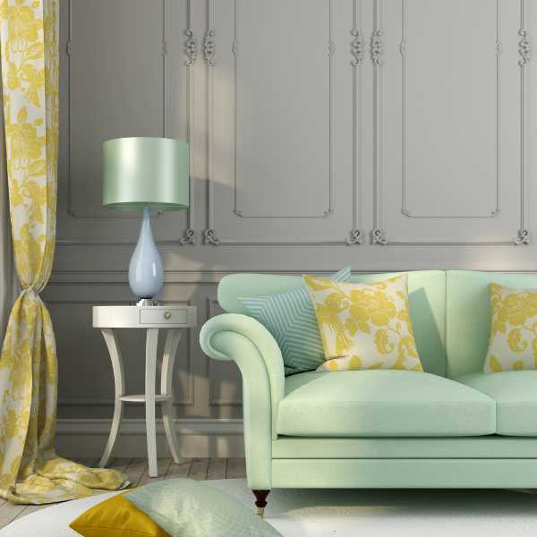 Throw pillows, sage green couch, lamp on a stool, yellow floral curtain and gray wall background. 