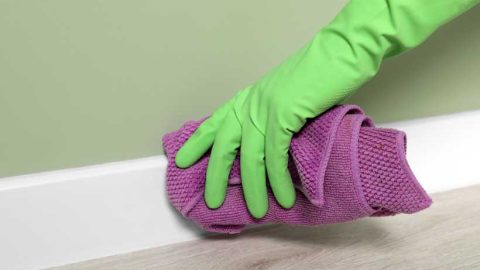 Someone cleaning a white baseboard with a rag - Featured image for 