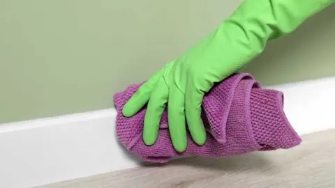 Someone cleaning a white baseboard with a rag - Featured image for