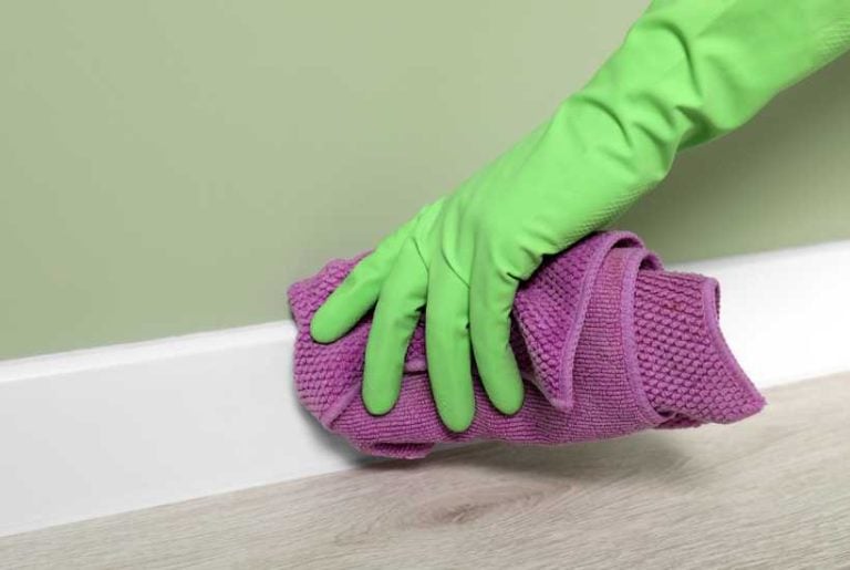 Someone cleaning a white baseboard with a rag - Featured image for "How to clean baseboards" blog post.